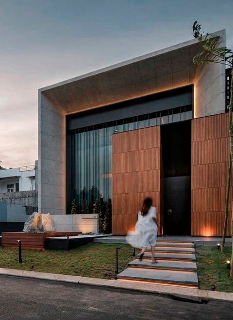 A figure ascending the lit stone threshold of an ARCTURUS residence at dusk